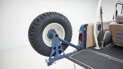 Spare tire mounted on the back of Classic Ford Bronco with blue body and beige interior