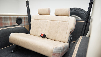 Rear bench seat inside Classic Ford Bronco upholstered in beige fabric with seatbelts