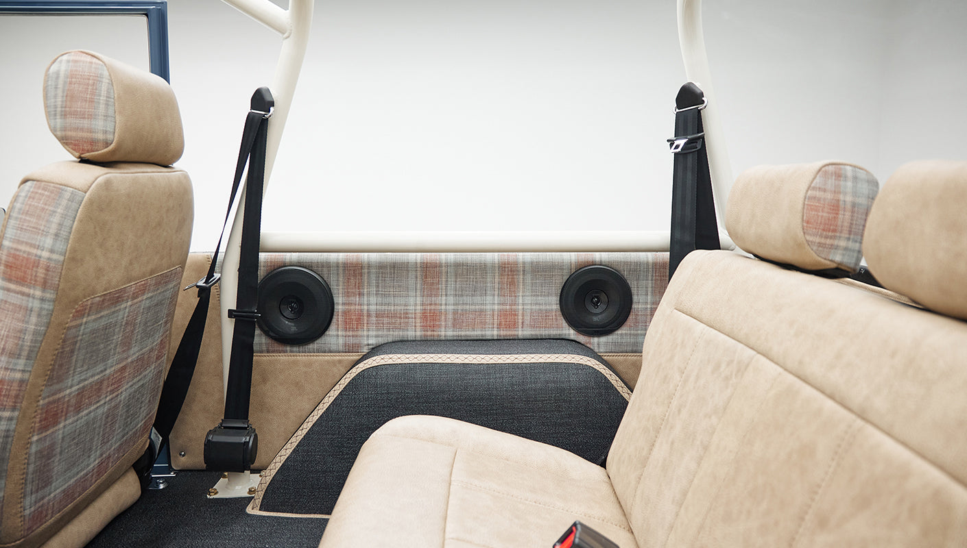 Interior rear seat and side door panel with tan and plaid upholstery, black seat belt and speakers