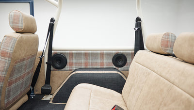 Interior rear seat and side door panel with tan and plaid upholstery, black seat belt and speakers