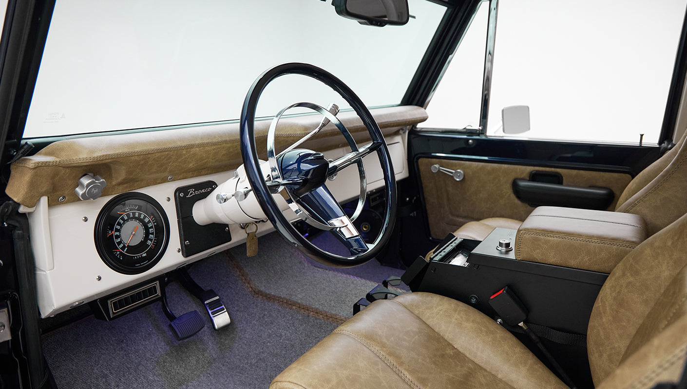 Driver's side view inside Classic Ford Bronco showing steering wheel, seats, and dashboard details
