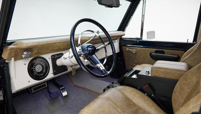 Driver's side view inside Classic Ford Bronco showing steering wheel, seats, and dashboard details