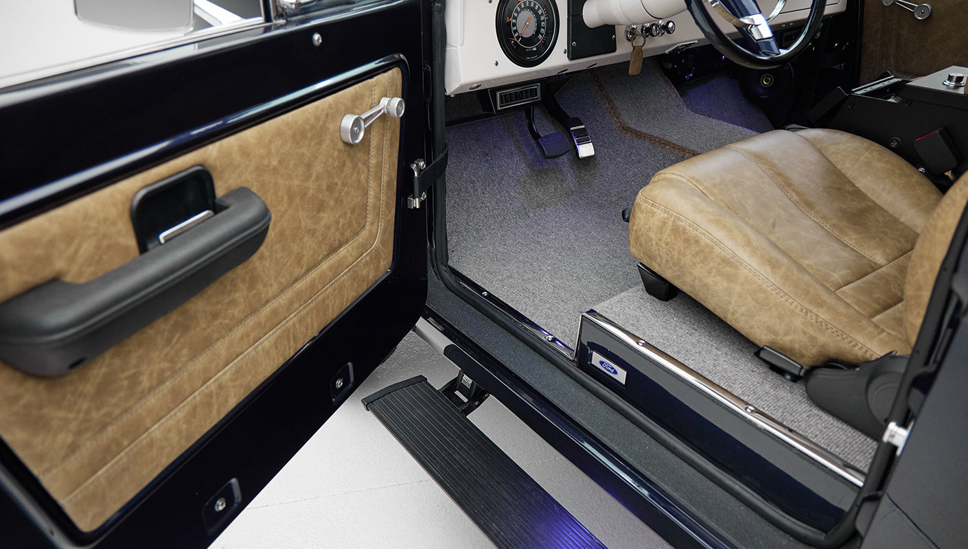 Front passenger seat area of Classic Ford Bronco with brown leather seat and open door revealing interior