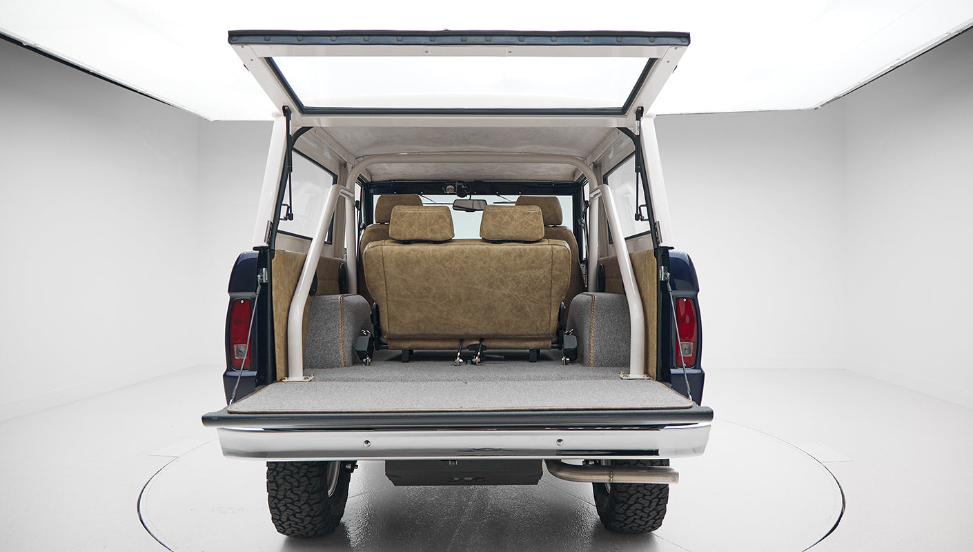 Classic Ford Bronco with rear open tailgate showing carpeted cargo area and tan leather rear seats