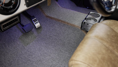 Close-up of Classic Ford Bronco driver side footwell with pedals and gray carpet with stitched accents