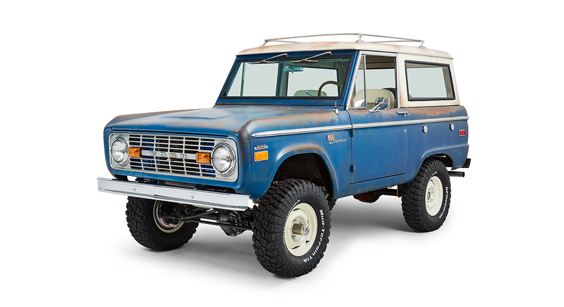 Front passenger-side angled view of a blue Classic Ford Bronco with white roof and off-road tires