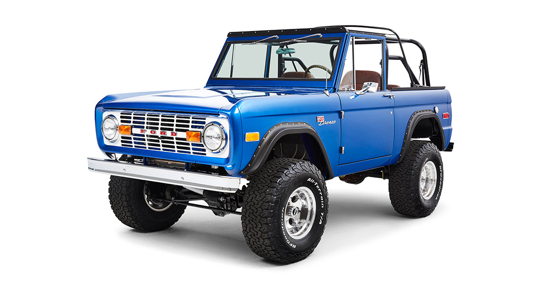 Front angled view of blue Classic Ford Bronco with black roll cage on white background