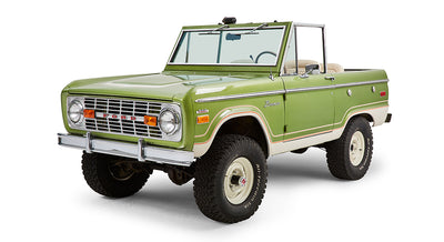Front driver angle view of a green Classic Ford Bronco convertible with white wheels and cream interior