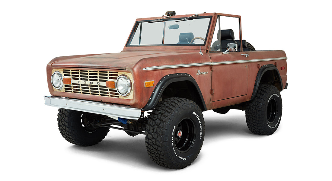Rust-colored Classic Ford Bronco front three-quarter view with chrome bumper and off-road tires.