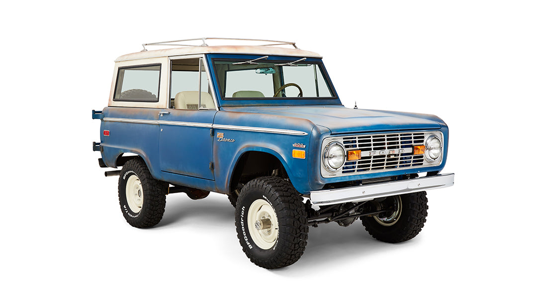 Front driver-side angled view of a blue Classic Ford Bronco with white roof and off-road tires