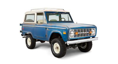 Front driver-side angled view of a blue Classic Ford Bronco with white roof and off-road tires