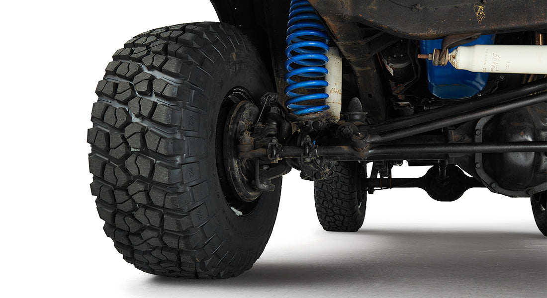 Close-up of front passenger side suspension with large off-road tire and blue coil spring
