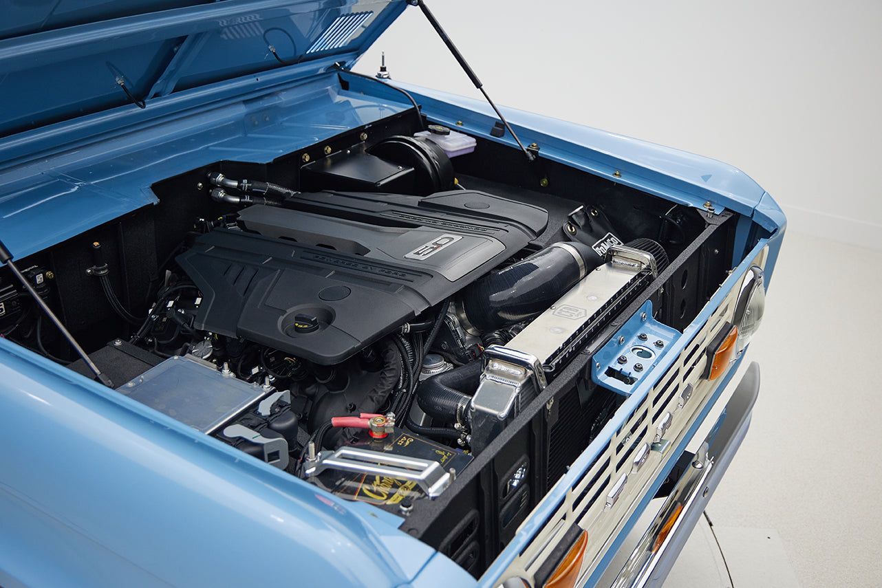 Engine bay of Classic Ford Bronco in Frozen Blue showing modern V8 engine components and radiator