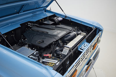 Engine bay of Classic Ford Bronco in Frozen Blue showing modern V8 engine components and radiator