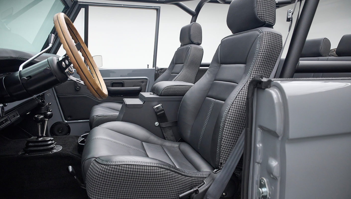 Front seats and dashboard inside Classic Ford Bronco with wood steering wheel and houndstooth seating