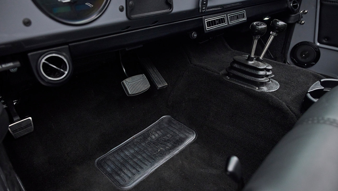 Pedals and floor area of Classic Ford Bronco interior showing black carpeting and shifter levers