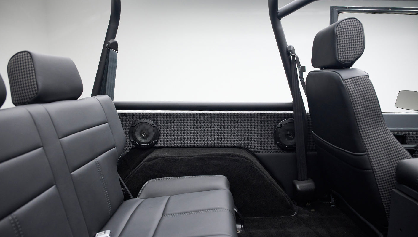 Interior side panel featuring two speakers and black leather rear seat with seat belts, roll cage visible