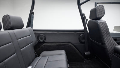 Interior side panel featuring two speakers and black leather rear seat with seat belts, roll cage visible