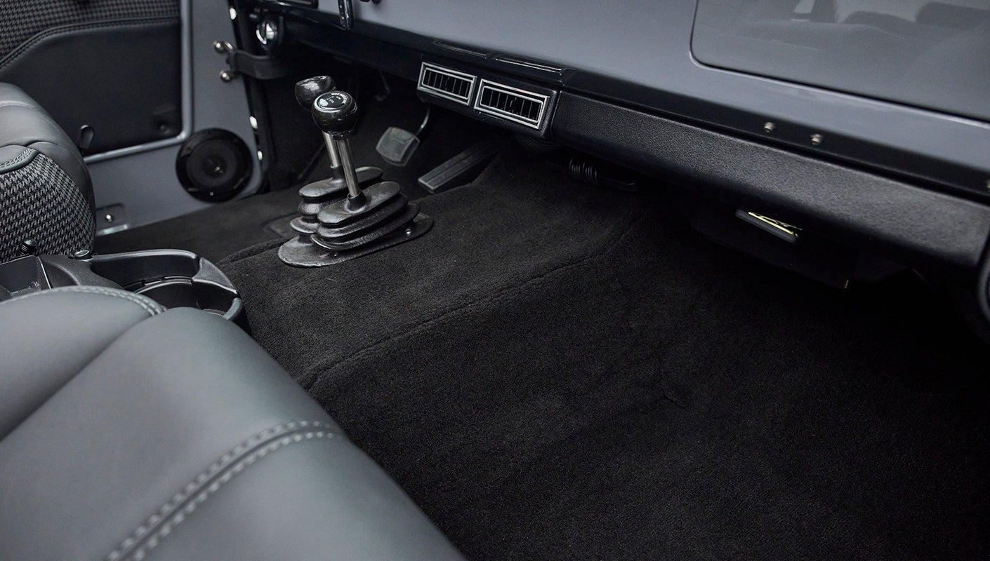 Rear passenger floor area with black carpet and visible manual gear shift levers in foreground