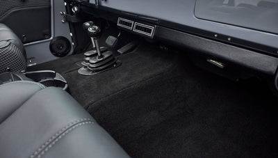 Rear passenger floor area with black carpet and visible manual gear shift levers in foreground