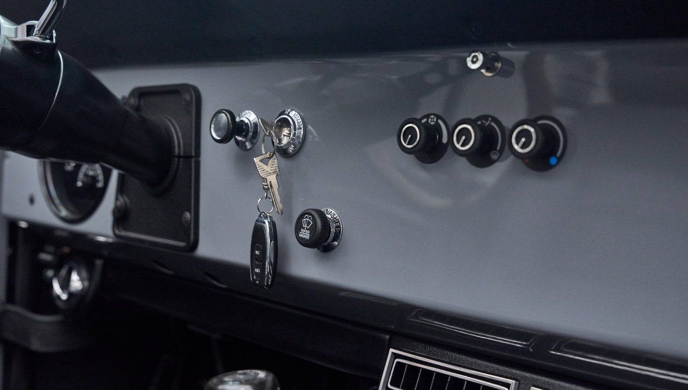 Dashboard section with ignition keys in switch, round control knobs, and gray painted surface inside Classic Ford Bronco