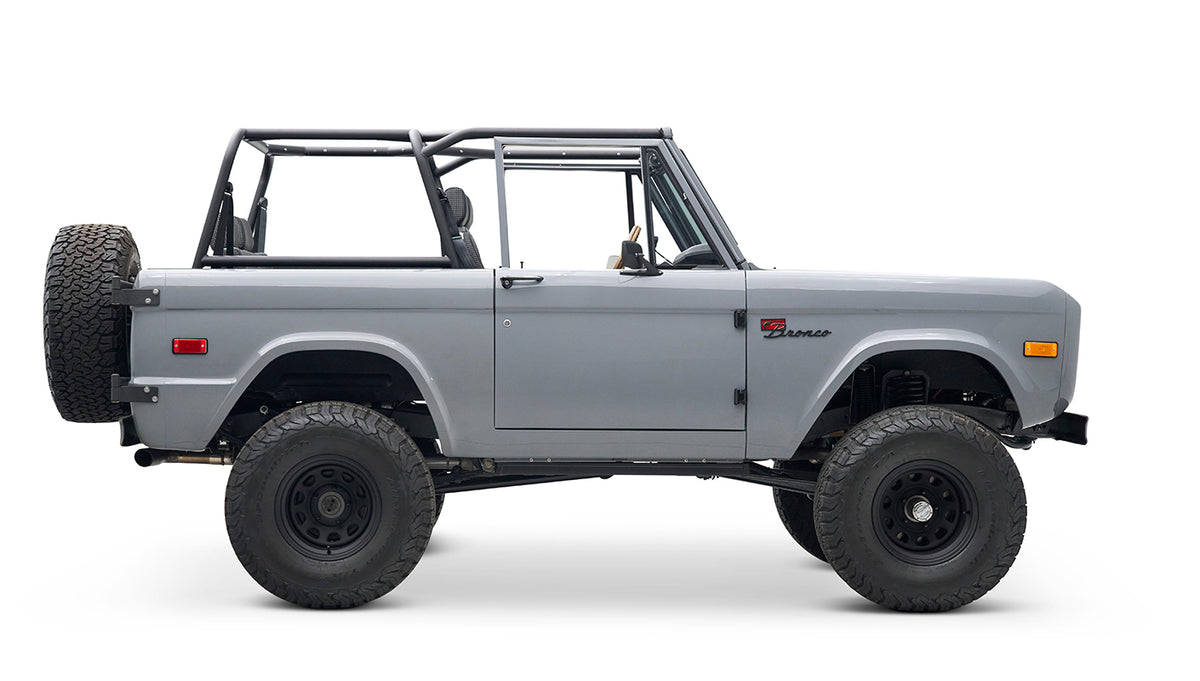 Side profile of a Classic Ford Bronco in gray with black wheels and roll cage, no roof