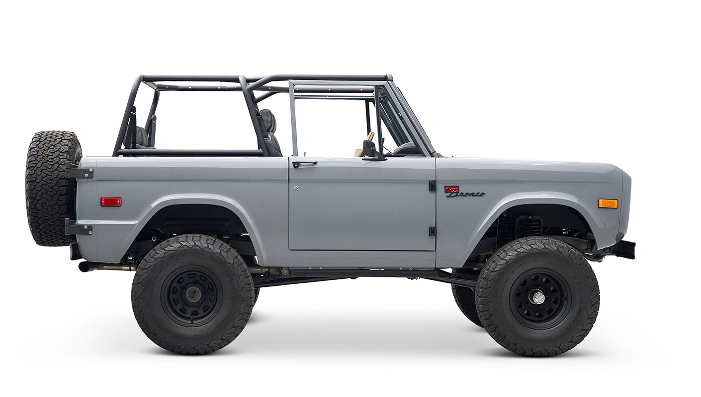 Side profile of a Classic Ford Bronco in gray with black wheels and roll cage, no roof