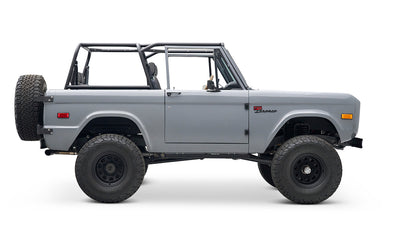 Side profile of a Classic Ford Bronco in gray with black wheels and roll cage, no roof