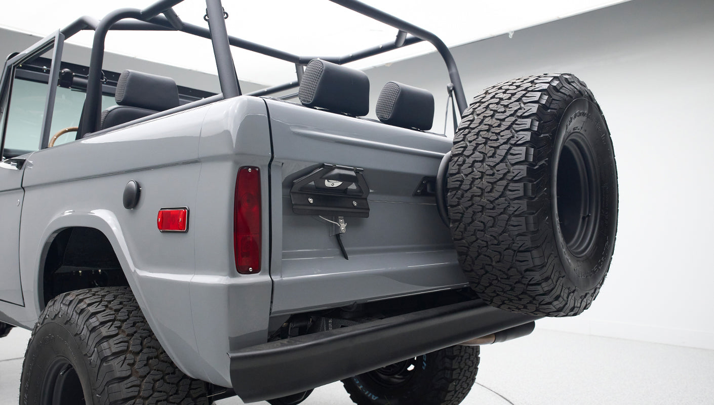 Rear view of gray Classic Ford Bronco showing tailgate, spare tire, and seating area in white studio.