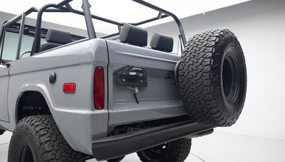 Rear view of gray Classic Ford Bronco showing tailgate, spare tire, and seating area in white studio.