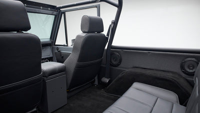 Gray Classic Ford Bronco interior showing seats with houndstooth and leather upholstery, seatbelts, and black floor.