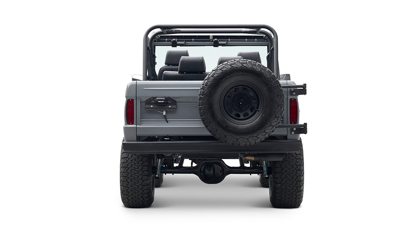 Rear view of a Classic Ford Bronco in gray with spare tire mounted on back, large tires, and roll cage