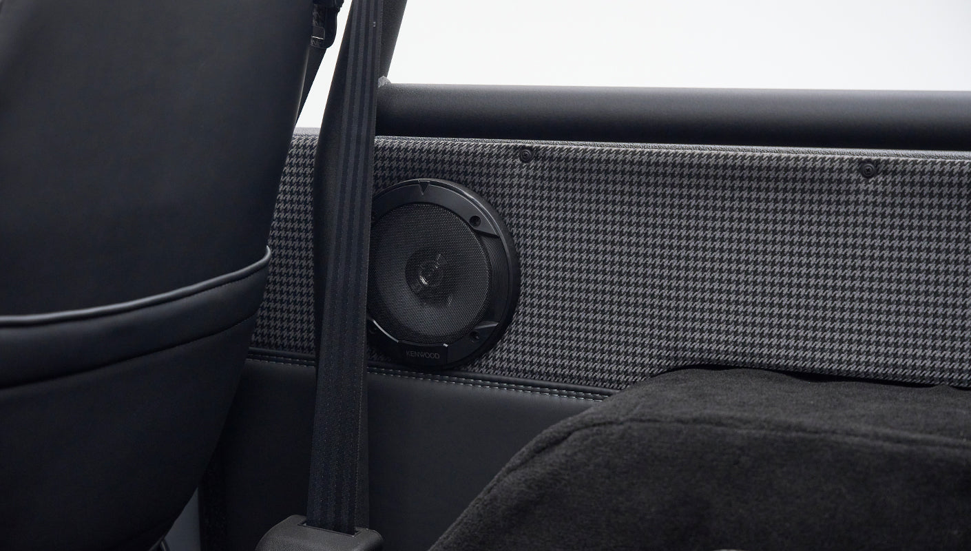 Kenwood speaker mounted on gray houndstooth patterned panel with seatbelt strap inside Classic Ford Bronco