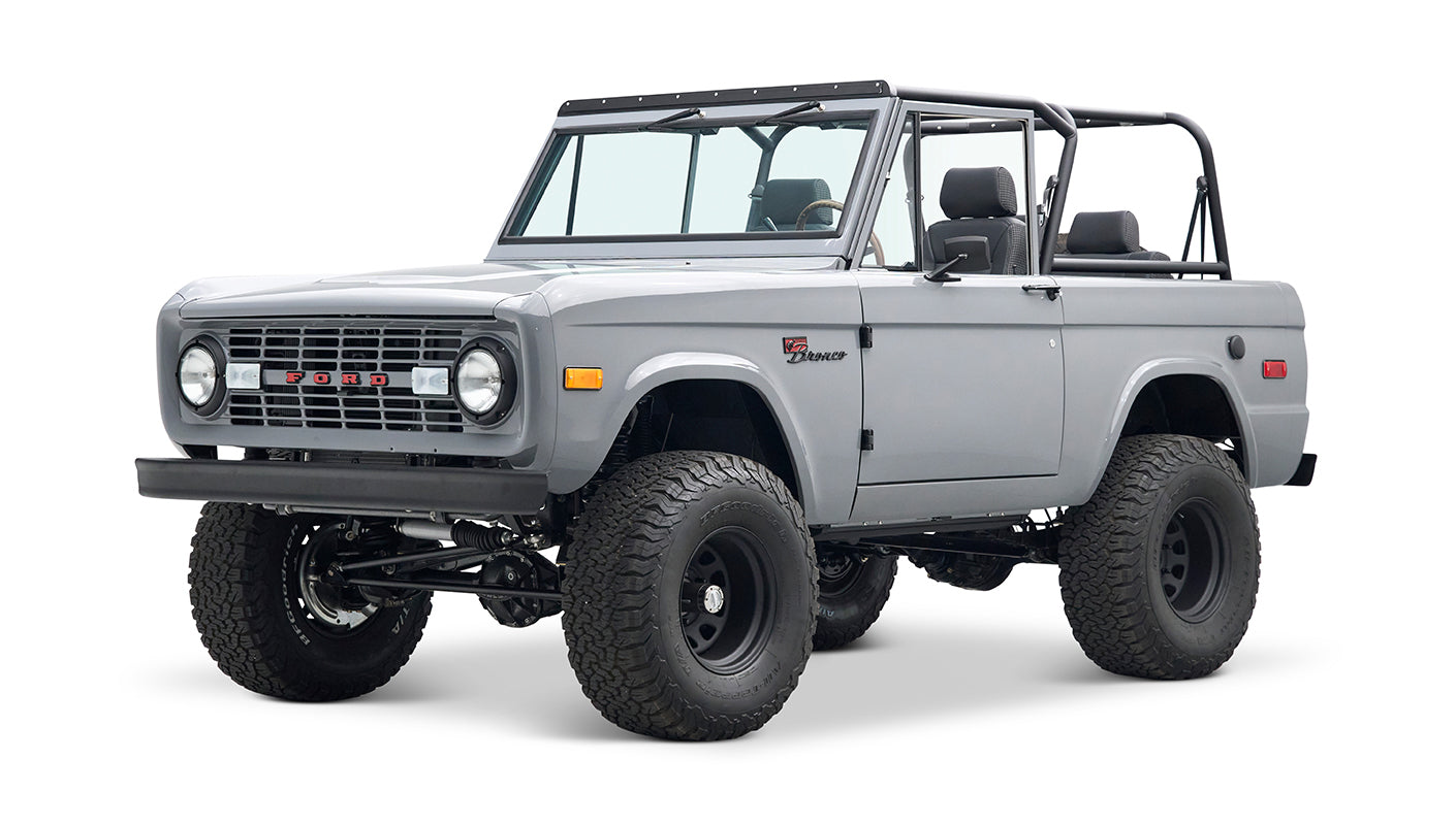 Classic Ford Bronco in light gray with off-road tires and black roll cage, side view