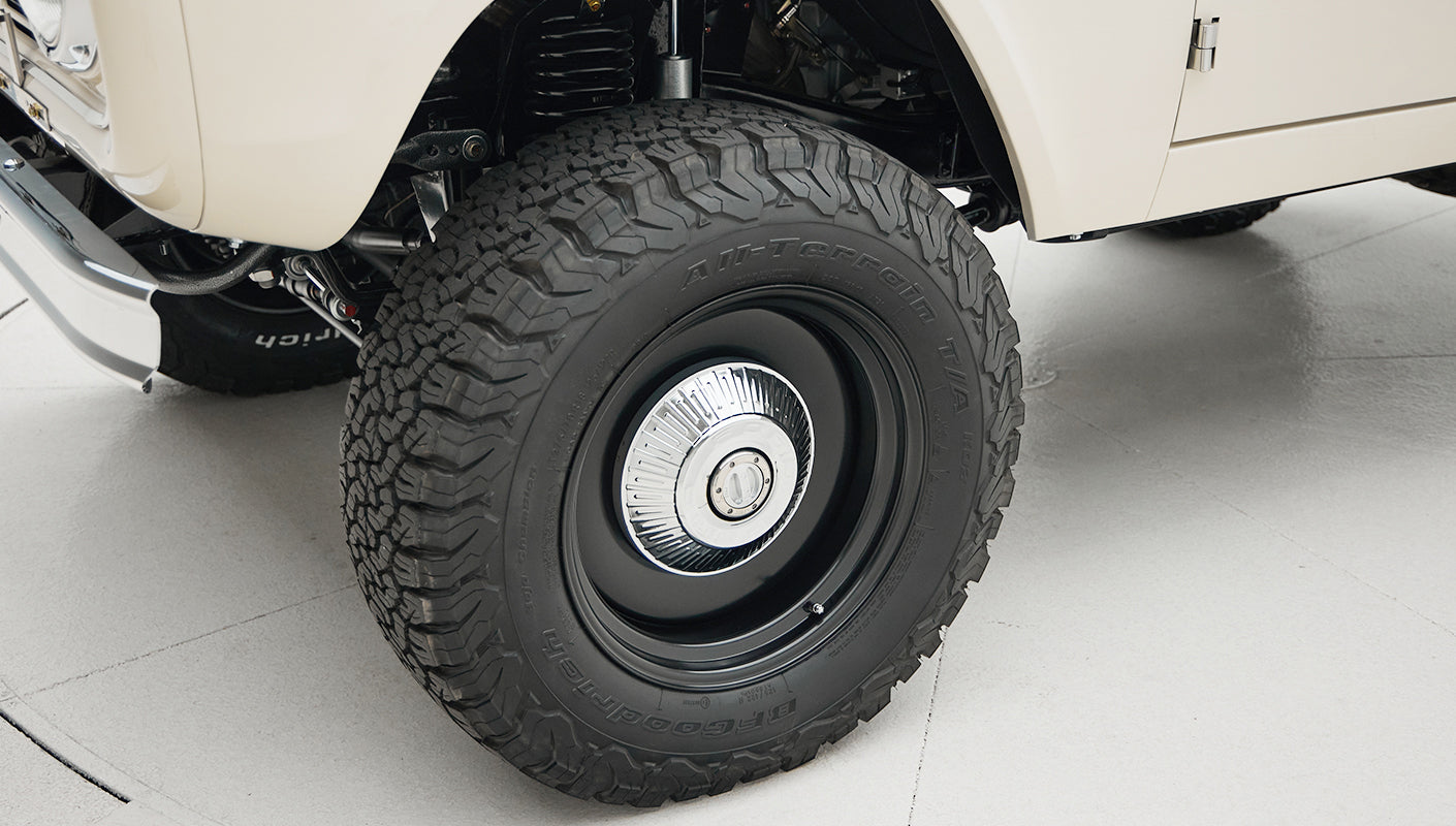 Close-up of all-terrain tire and suspension under a white Classic Ford Bronco