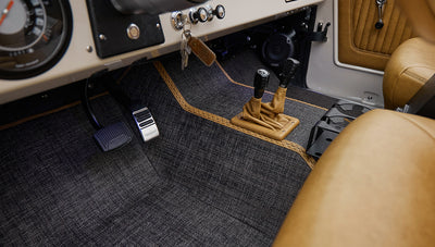 Footwell area of Classic Ford Bronco featuring pedals and gearshift with tan leather boot