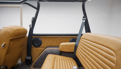 Interior side view showing rear tan leather bench seat and black roll cage in Classic Ford Bronco