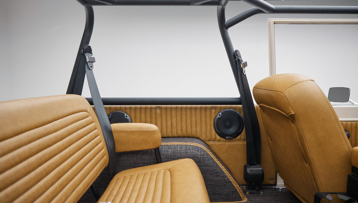 Rear interior view of Classic Ford Bronco with tan leather seats, roll cage, and side window