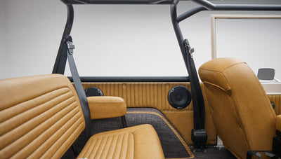 Rear interior view of Classic Ford Bronco with tan leather seats, roll cage, and side window