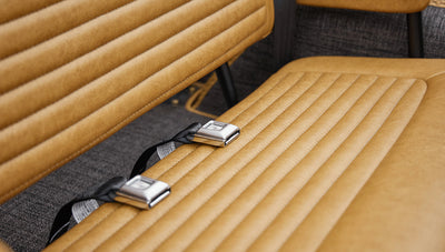 Tan leather bench seat with two metal seat belt buckles on gray carpet flooring