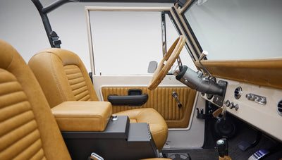Interior view of Classic Ford Bronco showing tan leather seats, door panel, and steering wheel