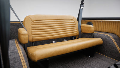 Side view of rear tan bench seat with armrests and seat belts inside Classic Ford Bronco