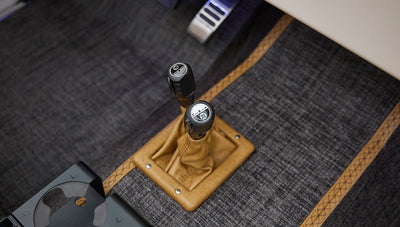 Tan leather gear shift and transfer case levers on gray carpet with tan stitched trim