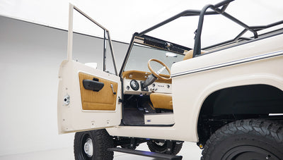 Open driver door of Classic Ford Bronco revealing tan interior door panel and seating