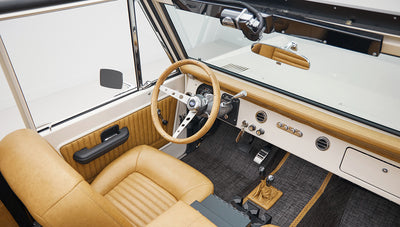Interior driver's seat with tan leather, wooden steering wheel, and beige dashboard in Classic Ford Bronco
