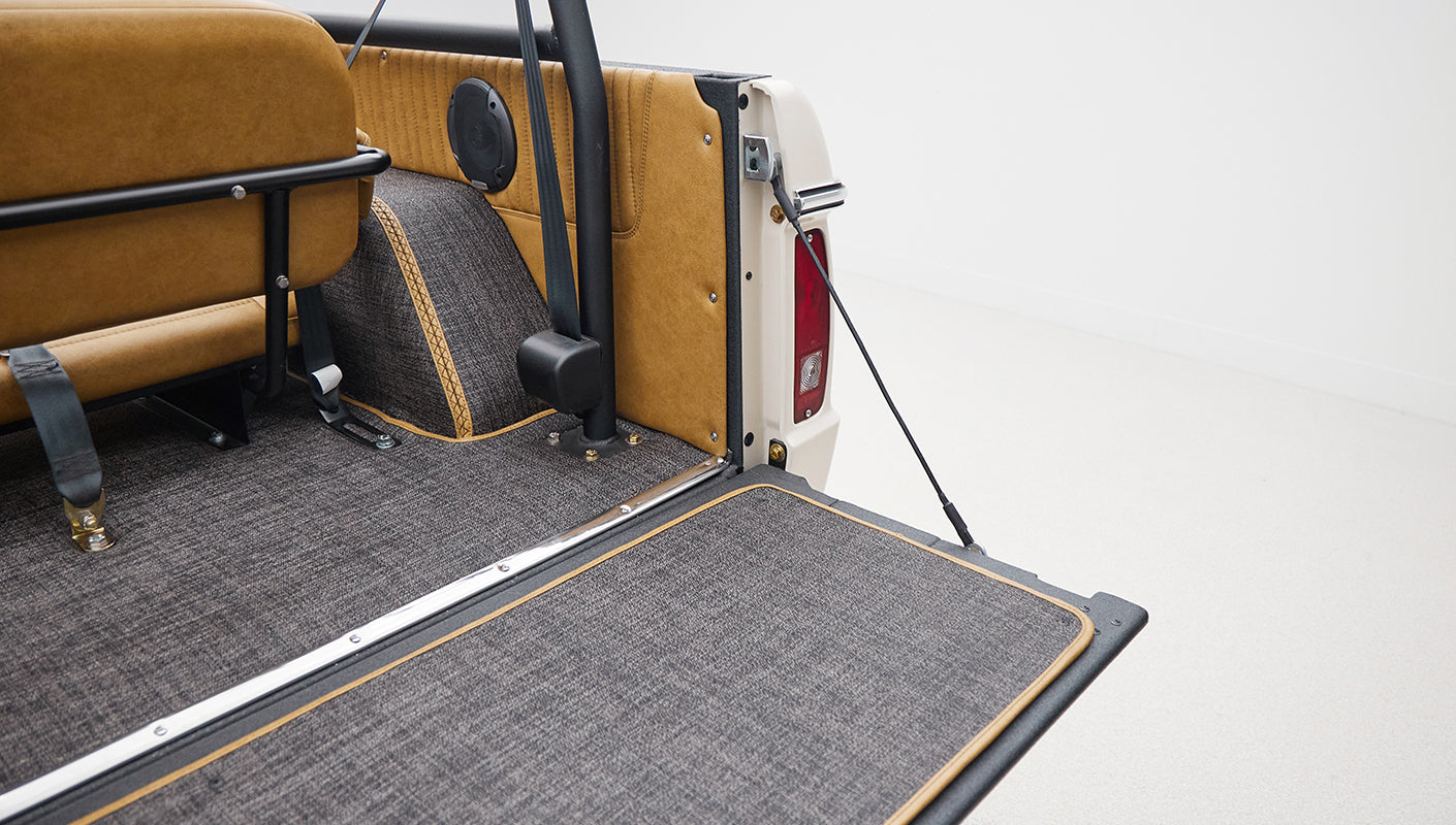 Rear cargo area with gray carpet and tan paneling, roll bar visible, and seat belts attached