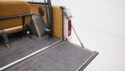 Rear cargo area with gray carpet and tan paneling, roll bar visible, and seat belts attached