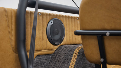 Close-up of black speaker mounted on tan interior panel above gray carpet inside vehicle