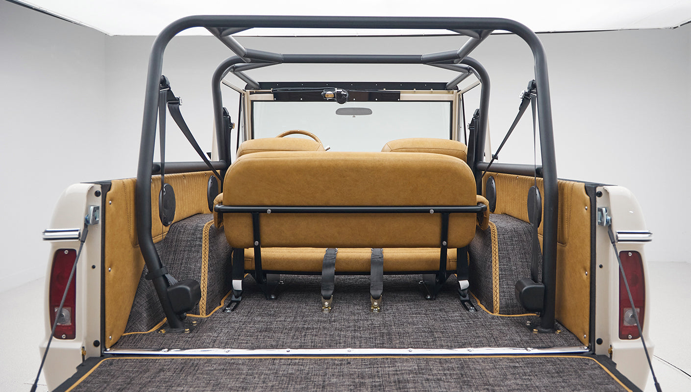 Rear view inside vehicle showing tan leather rear seats, roll bar, and gray carpeted flooring