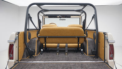 Rear view inside vehicle showing tan leather rear seats, roll bar, and gray carpeted flooring
